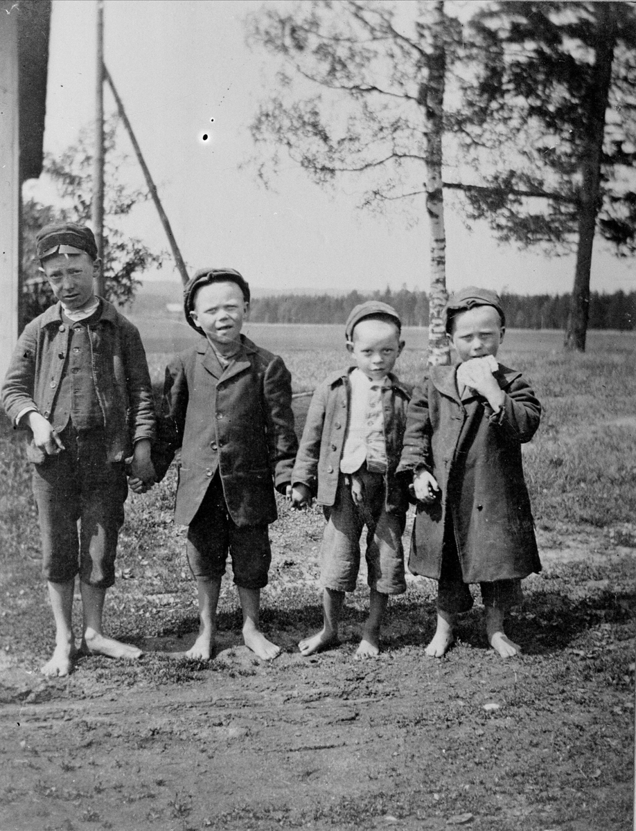 Fyra barfota pojkar i slitna kläder.
Påskrift på arkivexemplar: "Fattighjon från Jeppetorp fattiggård."
