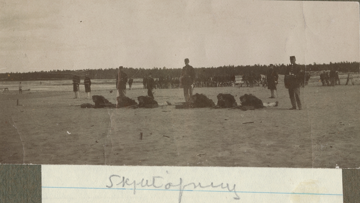 En grupp soldater över skytte i liggande skjutställning. Bakom skjutgruppen står instruktörerna.