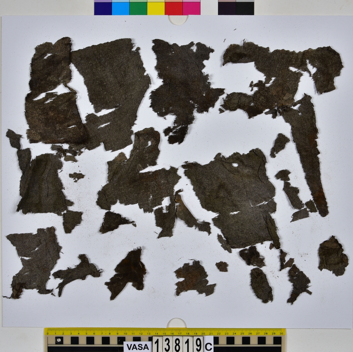Textilfragment, byxa.
125 fragment uppdelade på fyndnummer 13819a-d.
Fnr 13819a består av 44 fragment av ull vävt i tuskaft och valkat på ena sidan. En del av fragmenten har originalkanter med sömmar och fållar.
Fnr 13819b består av 35 fragment av ull vävt i tuskaft. En del av fragmenten har originalkanter med sömmar.
Fnr 13819c består av 40 fragment av ull vävt i tuskaft. En del av fragmenten har originalkanter med sömmar. Fragmenten är mycket sköra.
Fnr 13819d består av 6 fragment mönstervävt band av ull.