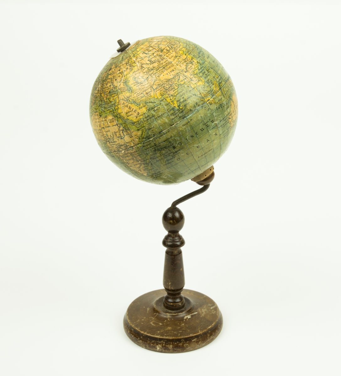 Jordgloben sitter på en brun träfot. Själva globen är gjord av papp. Rakt igenom globen går en metallaxel. På metallaxelns topp sitter en mutter.