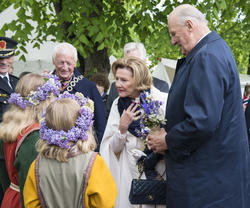 Hamar ordfører Einar Busterud står sammen med Dronning Sonja og Kong Harald, blomsterpiker med krans i håret med ryggen til kamera.