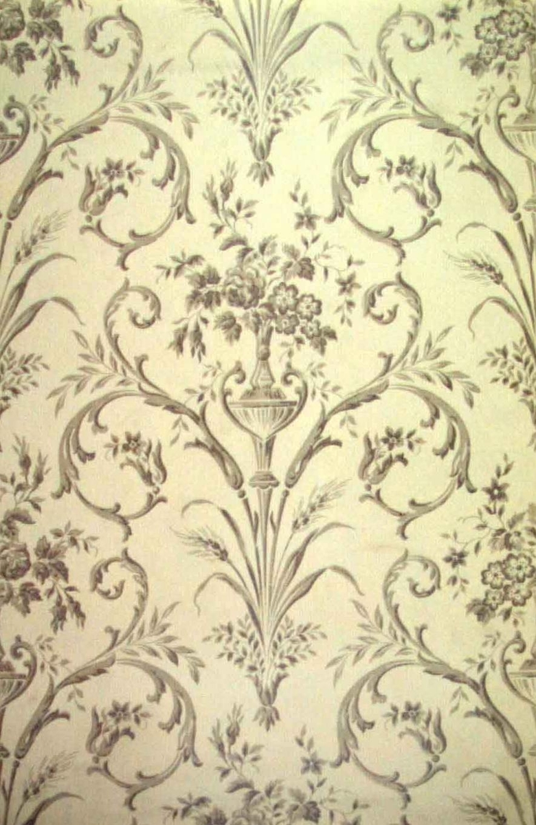 Ett ytfyllande mönster med blomsterurnor dekorerade med arabesker i diagonalupprepning. Tryck i två ljusgrå nyanser på en cremevit bakfgrund.