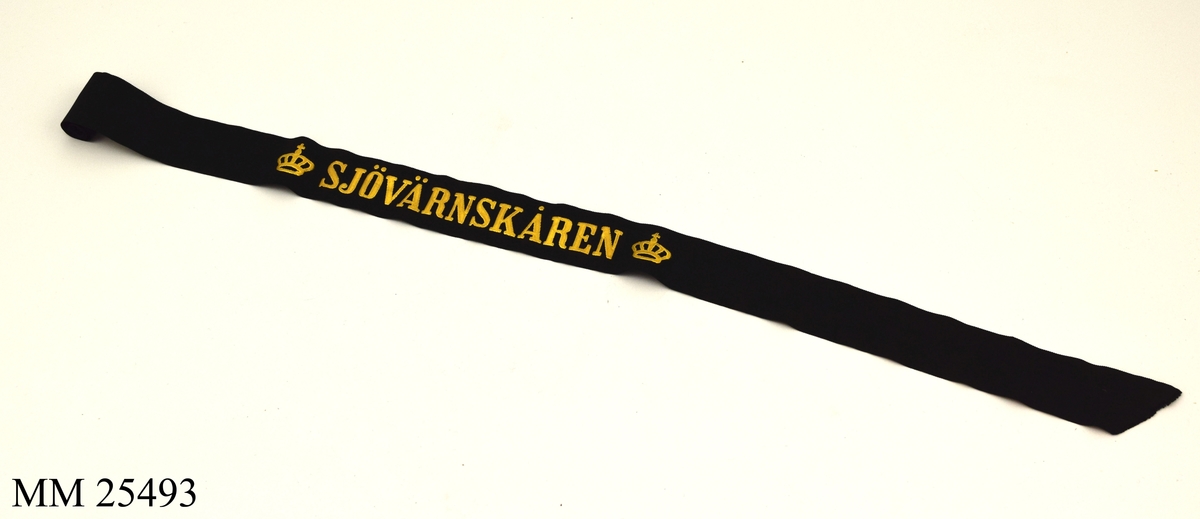 Möss band av svart sidenrips. Guldfärgad text med texten "Sjövärnskåren" med två kronor på vardera sida.