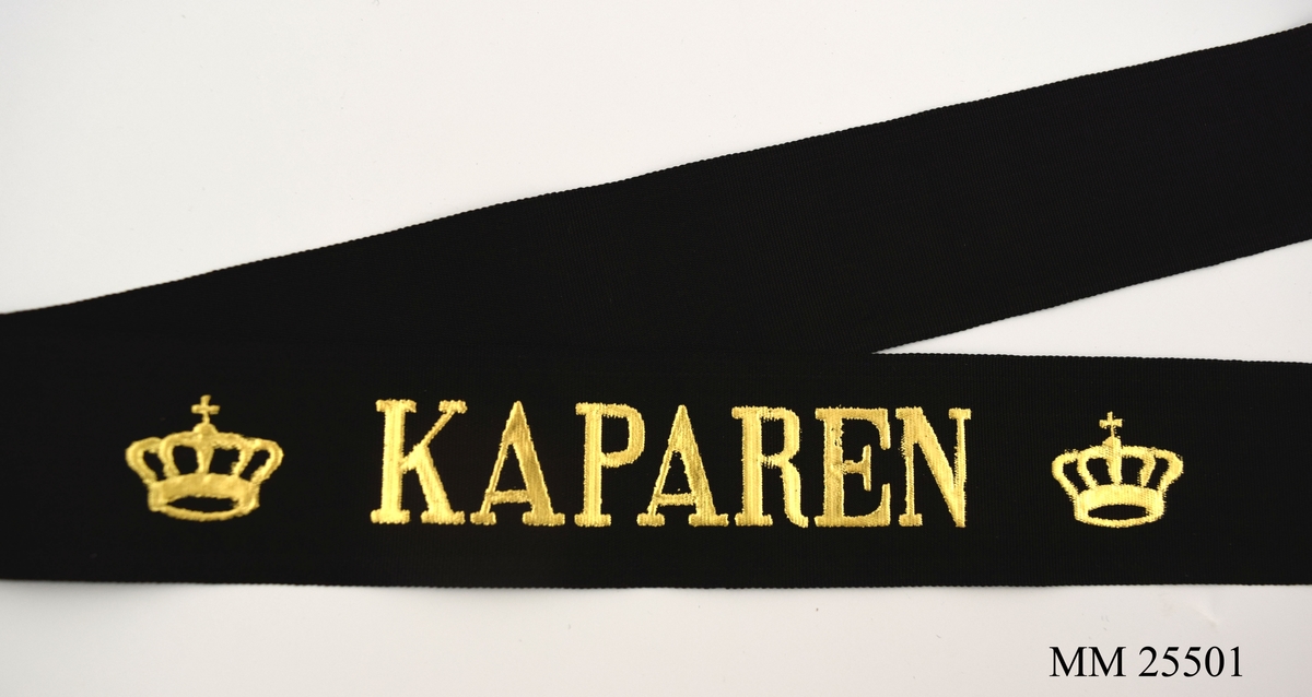 Mössband av svart sidenrips. Guldfärgad text, "Kaparen", med två kronor på vardera sida.