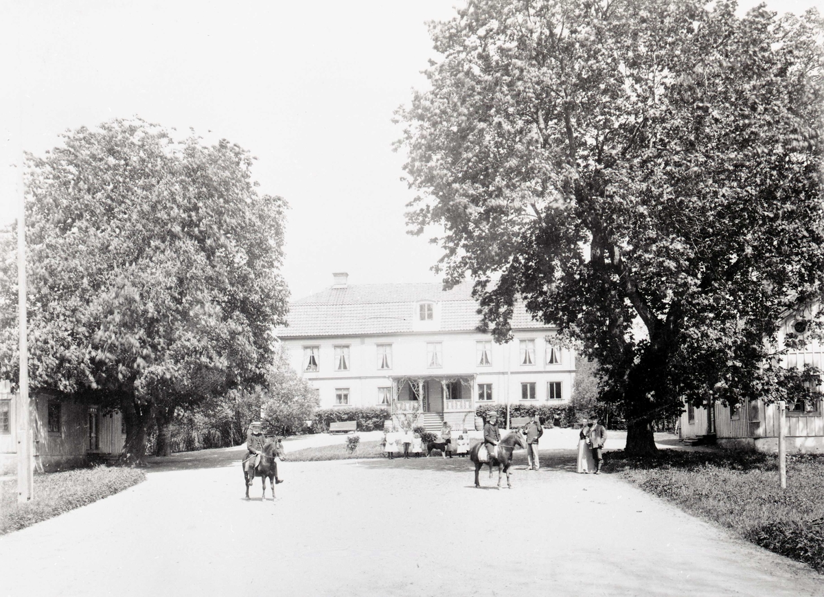 Huvudbyggnaden med folk framför och två pojkar som rider på Ölandshästar. Paret till höger är (troligen) Christian Wilhelm Liedholm med maka Anna Thomasine Elisabeth Liedholm.