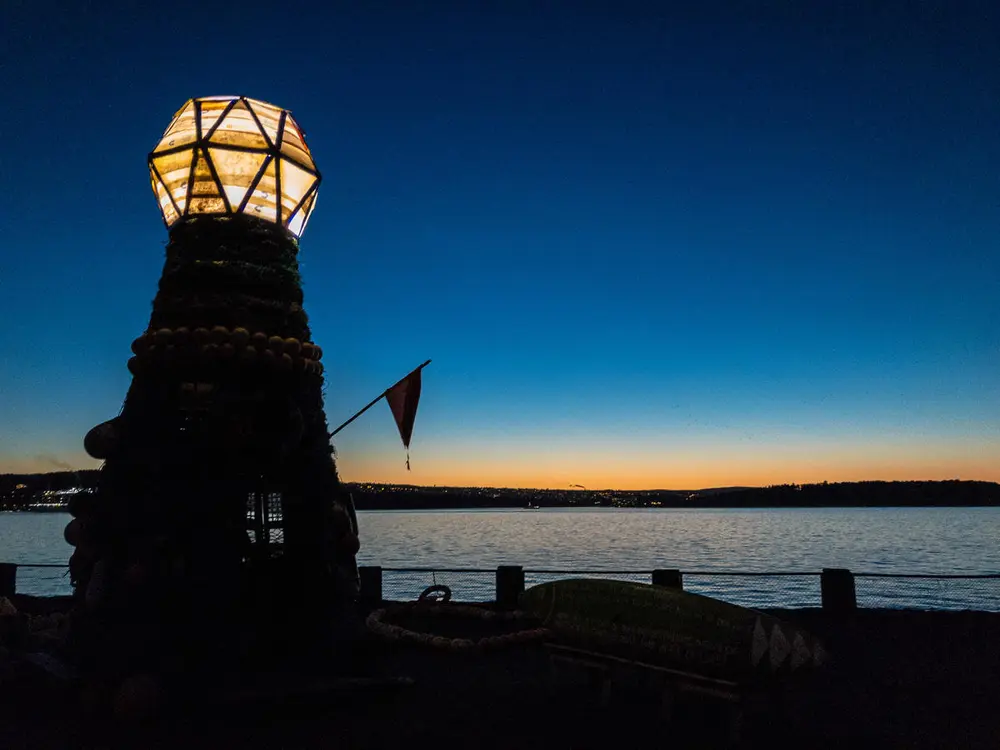 Kveldsstemning ved Fyrtårnet ved Norsk Maritimt Museum, laget av søppel fra havet. Mørkeblå himmel, antydning til solnedgang.