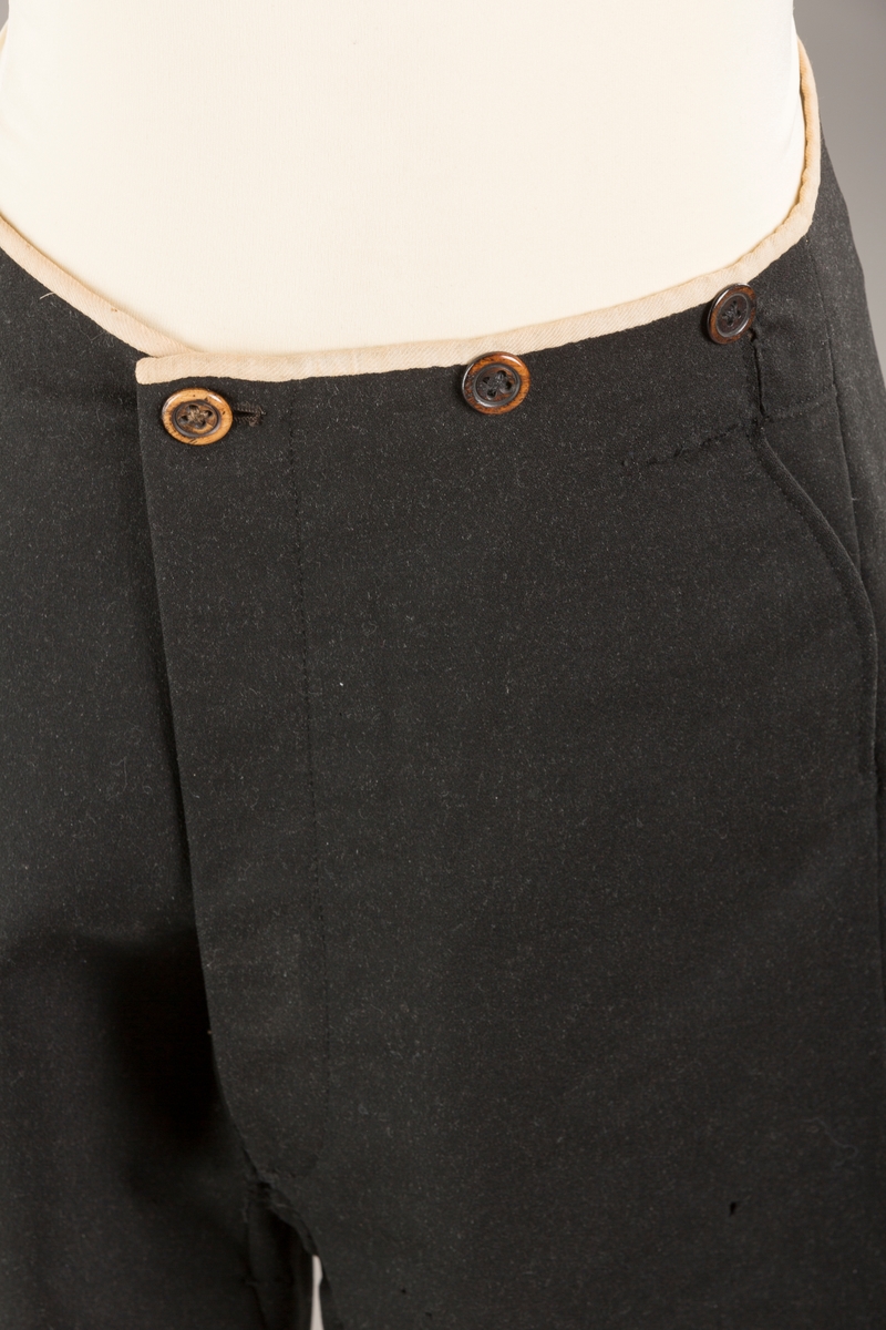 Form: Bena utvidet nederst. Lerretskant rundt livet, spensel i ryggen, mangler spenne i sepnsel?
Delvis foret. To lommer. 5 knapper, mangler en knapp.