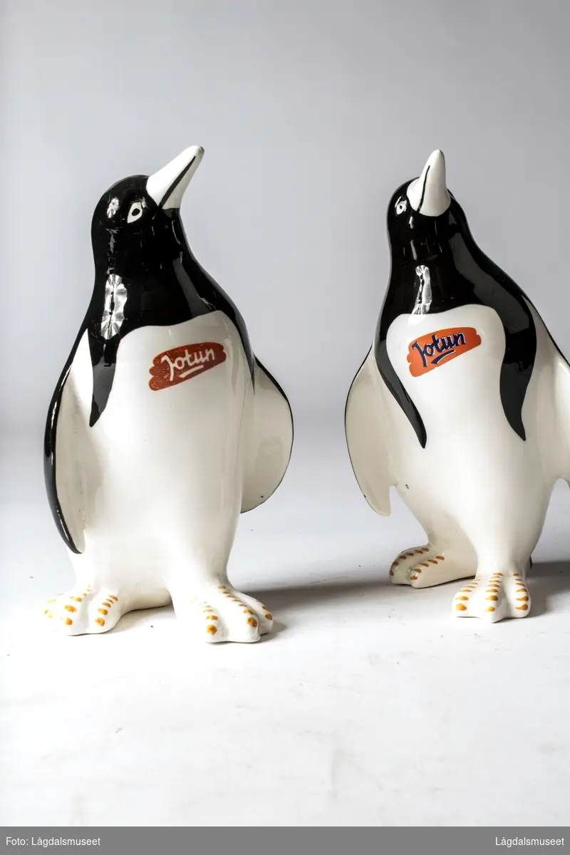 Pingvin i fajanse med firmalogo for Jotun i hvite bokstaver på rødbrun bakgrunn på brystet til pingvinen.