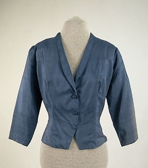 Jacka av blått shantungsiden tillhörande klänning 106163:1.
Knäppes med tryckknappar, tre st klädda knappar som dekoration.
Fodrad med ett blått viskosfoder.
Sydd av givaren på 1950-talet.