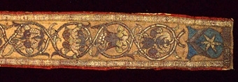 Besättning till korkåpa, i ljust gulaktigt brun (tidigare röd) damast, med cirkelformade broderier, utförda i guld- och silverlan. 
Vapensköldar avslutar broderiet i vardera änden. Där under namnförkortningarna 
MAGN(US)  AMBÂ´NI (Magnus Ambjörnsson, kanik i Skara1508-1510), resp. 
JOH(ANNE)S  DECA(NUS)  SCAR (Johannes Johannis, dekan i Skara från 1505). 
Besättningen är ett Vadstena arbete. 

Litteratur:
"Medeltida vävnader och broderier i Sverige" av A. Branting och A. Lindblom, del 1, sid 98 och plansch 62. 
"Västergötland, kyrklig konst under senmedeltiden" av Ernst Fischer sid 148, fig 110-111.
"Medeltida textilier i Skara Domkyrka" av Inger Estham. sid 379.