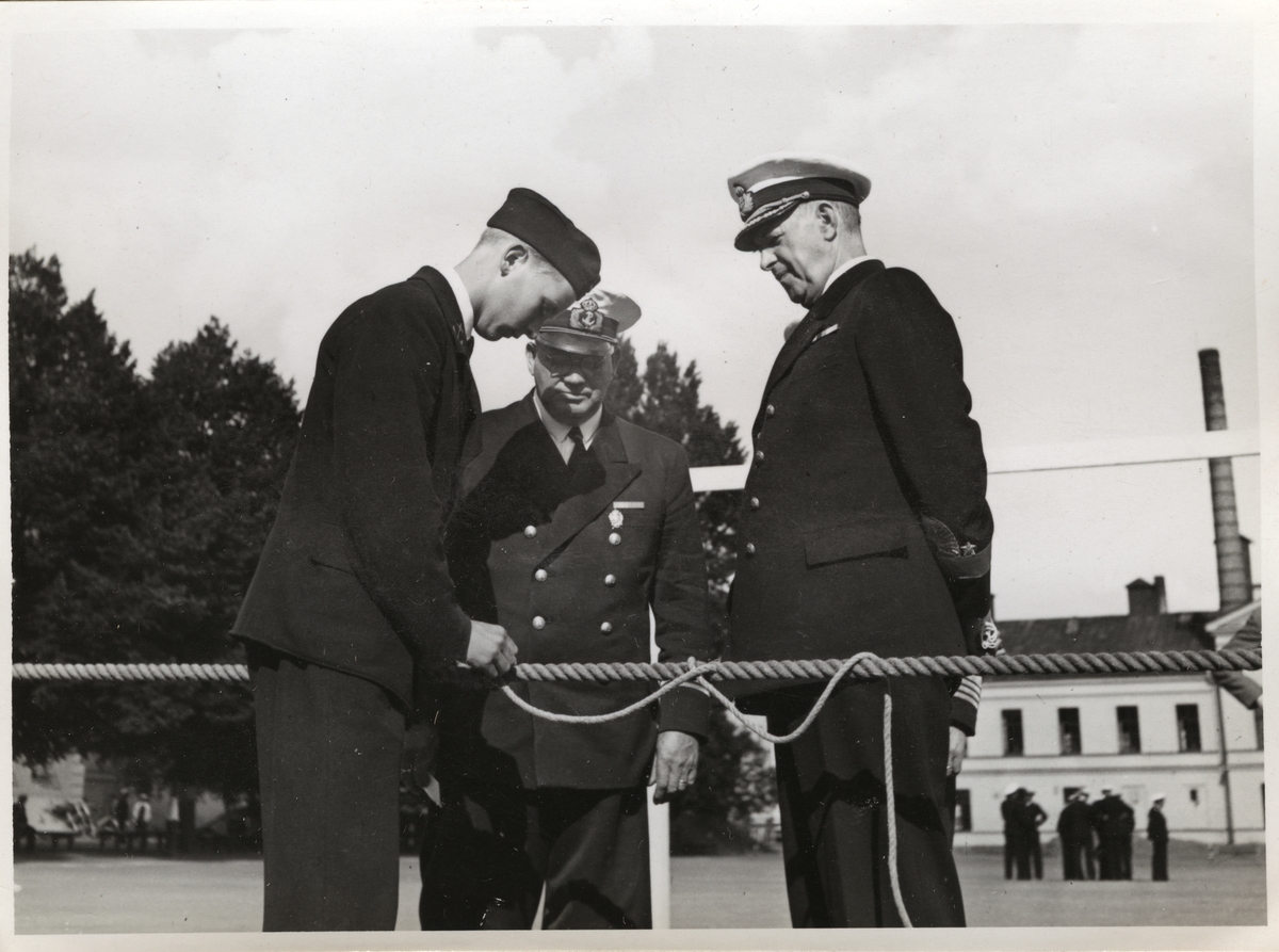 Bilden visar viceamiral Fabian Tamm och en kommendör i samtal med en rekryt som slår en stek runt en tampa.