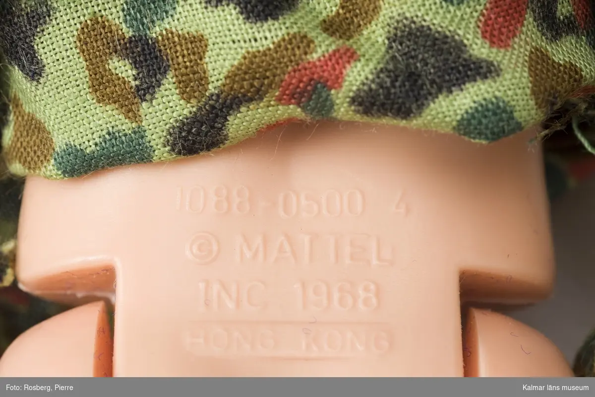 KLM 44315:3 Docka av plast. Klädd i militärkläder, hjälm och vapen, av textil och plast. Modellnamn: Ken 1088-0500 4. På ryggen text: 1088-0500 4 c Mattel, INC 1968, Hong Kong. På halsens baksida: c 1968 Mattel INC. Datering: 1968-70-tal.