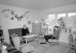 Foto av to kvinner sittende i en dagligstue. Bildet er regis