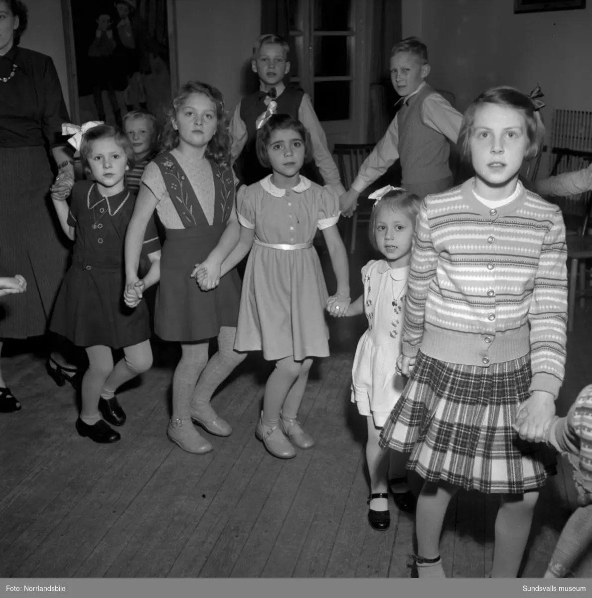 Barnjulfest, julgransplundring, i Sundsvalls Folkets hus. En liten flicka spelar dragspel och långdans med glada barn.