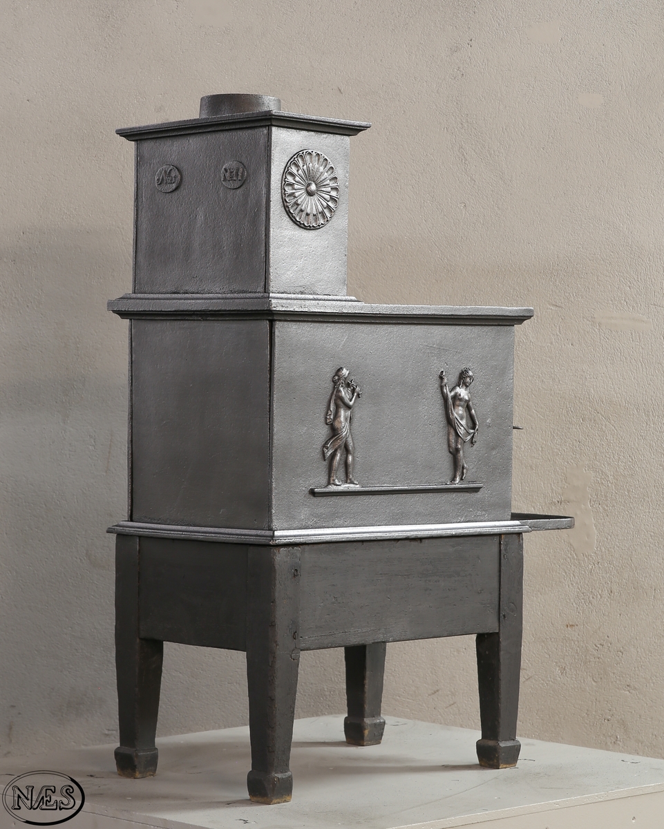 Kokeovn med to muser på enkel profillist. En fløytespillende og en dansende. Begge med draperier. Kokeanretning i topplaten til 1.etg. Ovnsdør på kortside. Rosett på begge sideplatene 2.etg. Den ene er løs og fungerer som ventil. Innskrift på frontplate og bakplate 2.etg. Røykuttak i toppen.