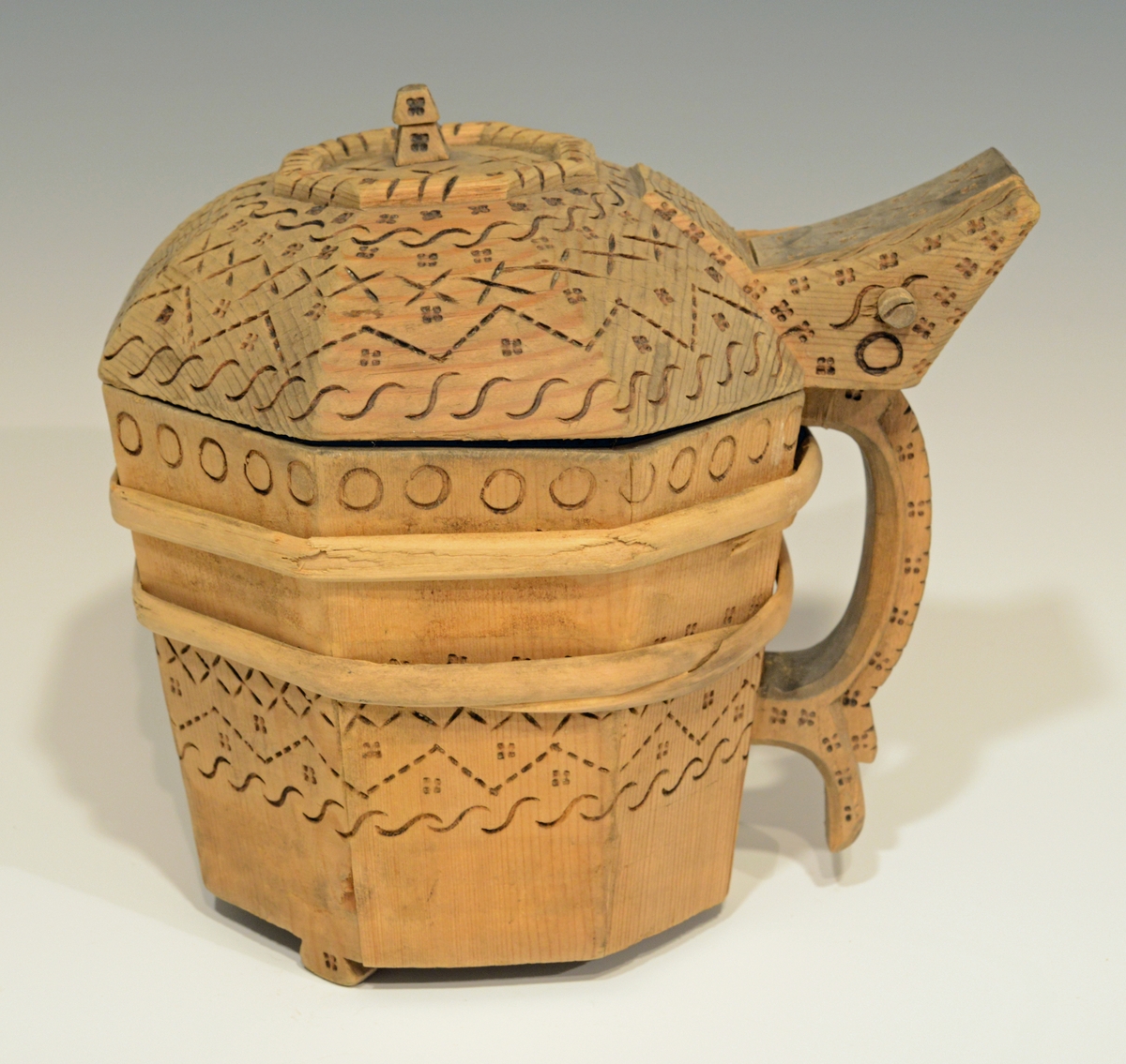 Fra katalog: Ottekantet smørkande og stav med hank og laak og tre smaa føtter, utvendig svimerket og en slynget ring oppe paa laaket, indvendig
rik rosette. Under staar brændemerket: A OSS 1823,