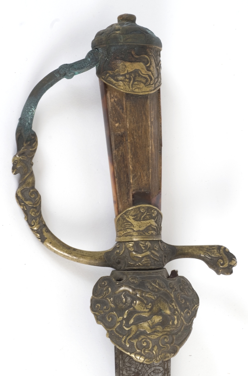 Knapp i form av hvelvet hette med dyreornamentikk og nedbøyd skjell på utsiden. Tregrep belagt med skilpaddeskall. Fremre parerstang går over i håndbøylen. Bakre parerstang ender i et stilisert dyrehode.  Nedbøyd skjell dekorert med dyremotiver på utsiden.
Enegget klieformet klingen med ryggslipning mot spissen. Klingen har en bred og en smal ryggstillt blodrand. Klingen har etset rankedekor på begge sider.
Lærbalg sydd på innsiden med messingbånd på toppen.