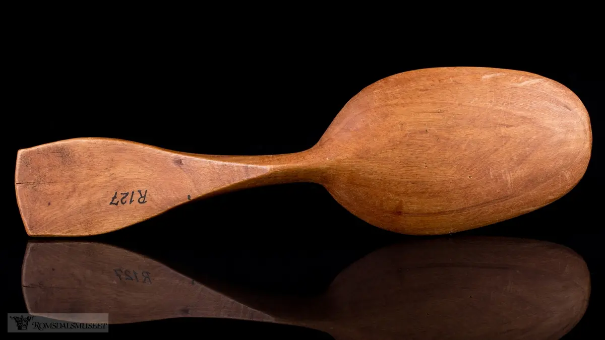 Enkelt formet og lakkert treskje uten dekor. Bredt flatt skaft og langt ovalt skjeblad.