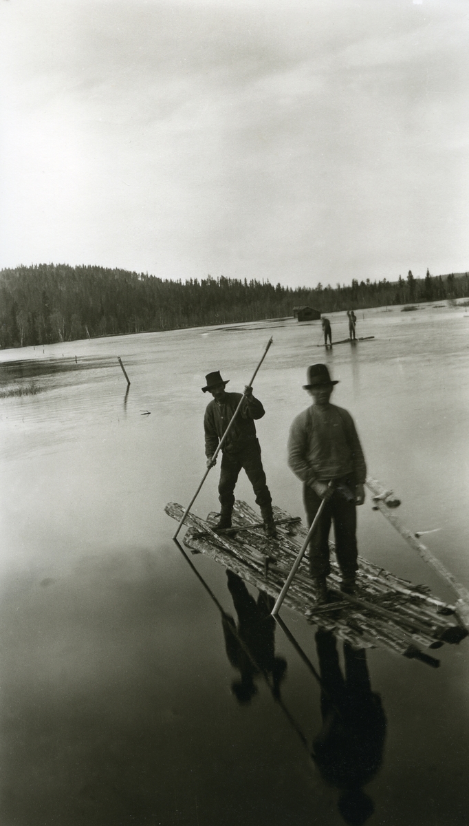 Menn på tømmerflåter ved Breidfloa (Grøna) øst for Galåsen. Løe i bakgrunnen.
Fra venstre (på den fremste flåten): Otto P. Flermoen (1901 - 1983) og Kristian Haugset (1889 - 1978)