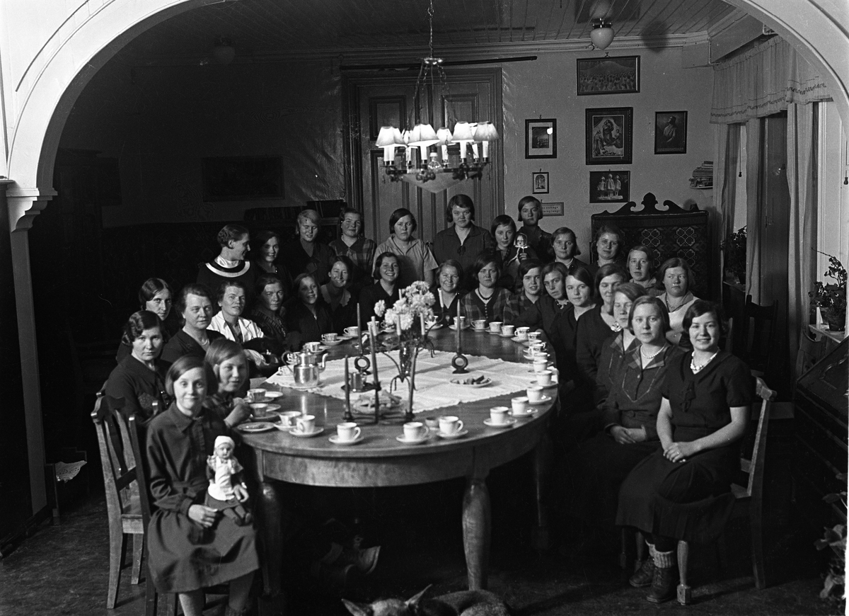 En rekke Kvinner/Jenter i ulik alder samlet rundt et stort bord dekket med kaffekopper. Hverken personer eller sted er identifisert.