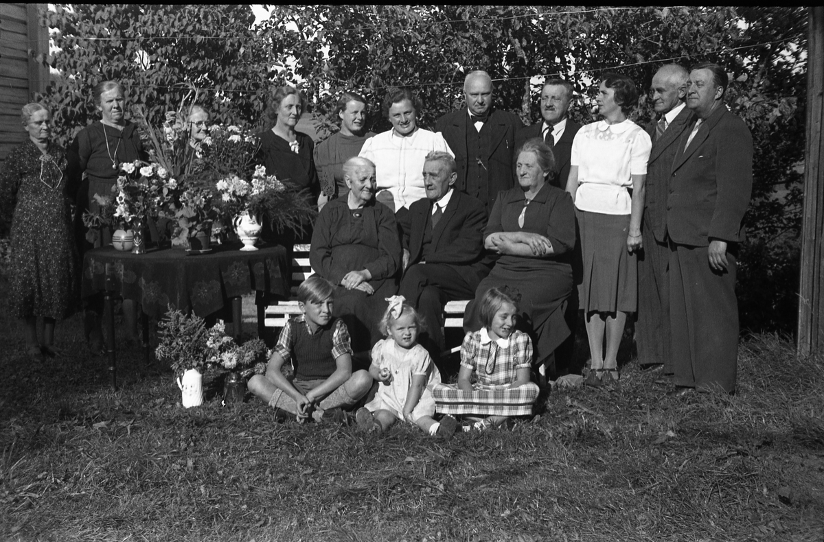 Antatt familieportrett tatt ved Dorte Hermansdatter Grønlis 90-års jubileum. Noen av personene er identifisert. Jubilanten sitter til venstre på krakken, og til høyre for henne ektemannen Mads Grønli. Lengst til venstre bak står Lina Grønli (svigerdatter). I midten bakerst med lys bluse står Dora Daarstad (barnebarn, f.Trannum), dernest hennes mann Einar Daarstad, og videre Jens Grønli, jubilantens sønn g.m. Lina. De øvrige er ikke identifisert.