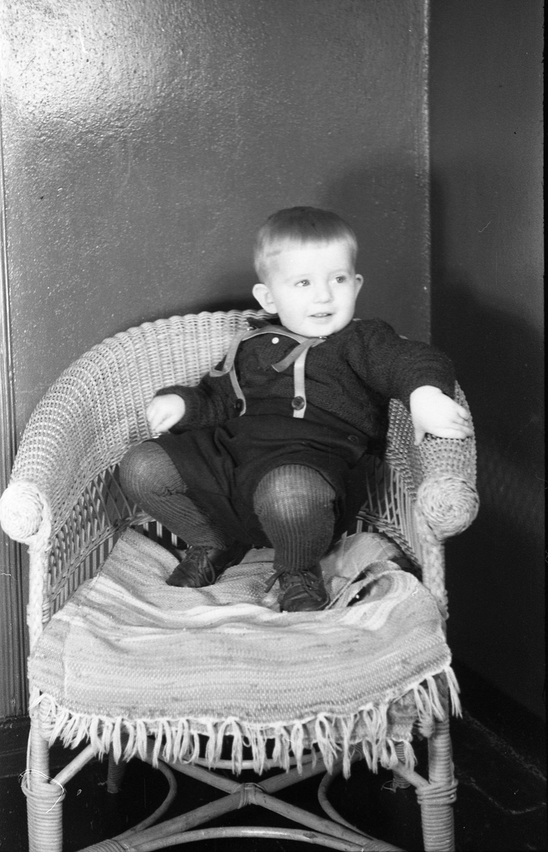 Portrett av et uidentifisert guttebarn som sitter i/står ved en kurvstol. Serie på 10 bilder.