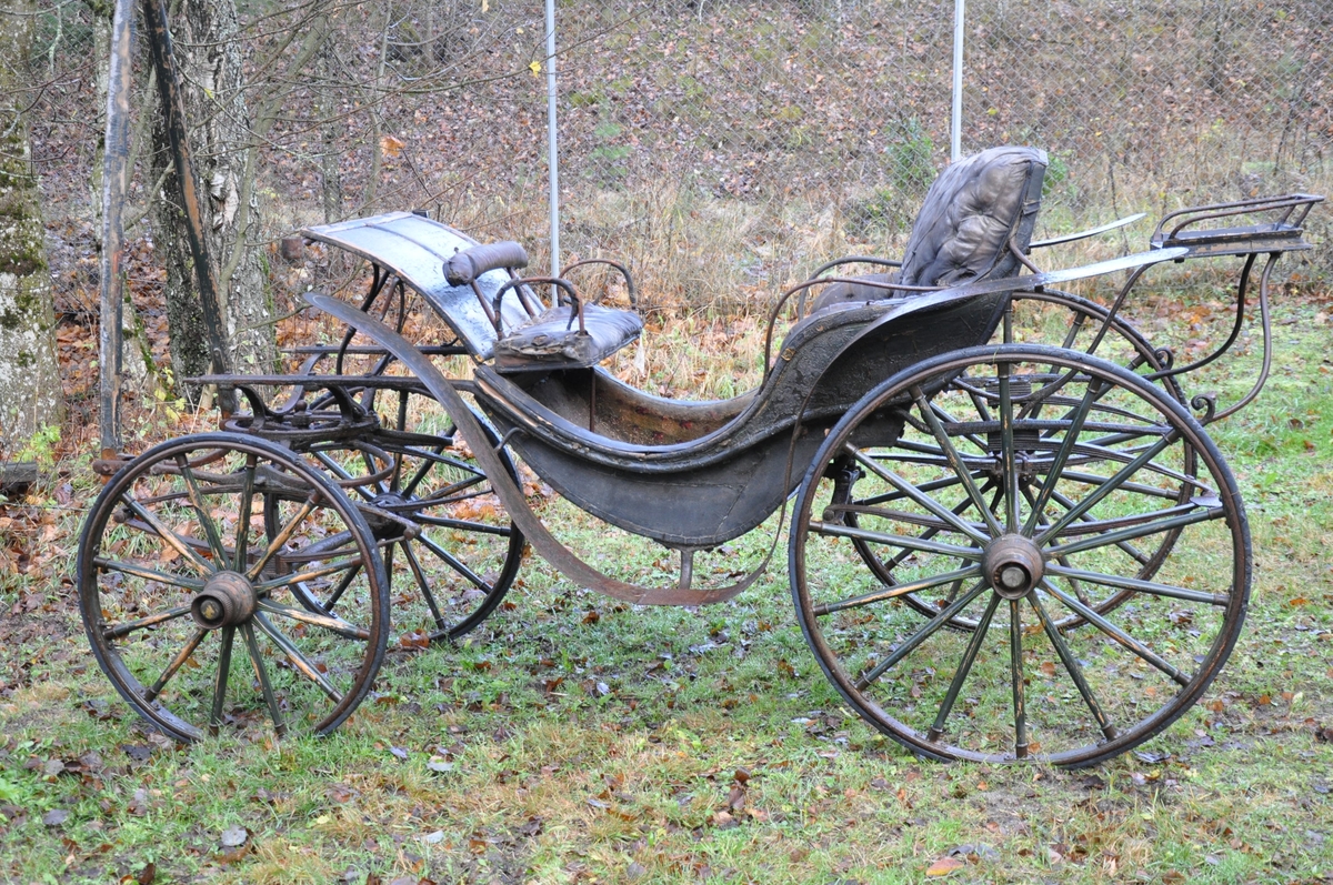 4-hjuls vogn for trekk med én hest. Trilletype. Spesielt stor fløy (skvettskjerm) . Lakeisete bakerst, stort hovedsete, lite motsete.