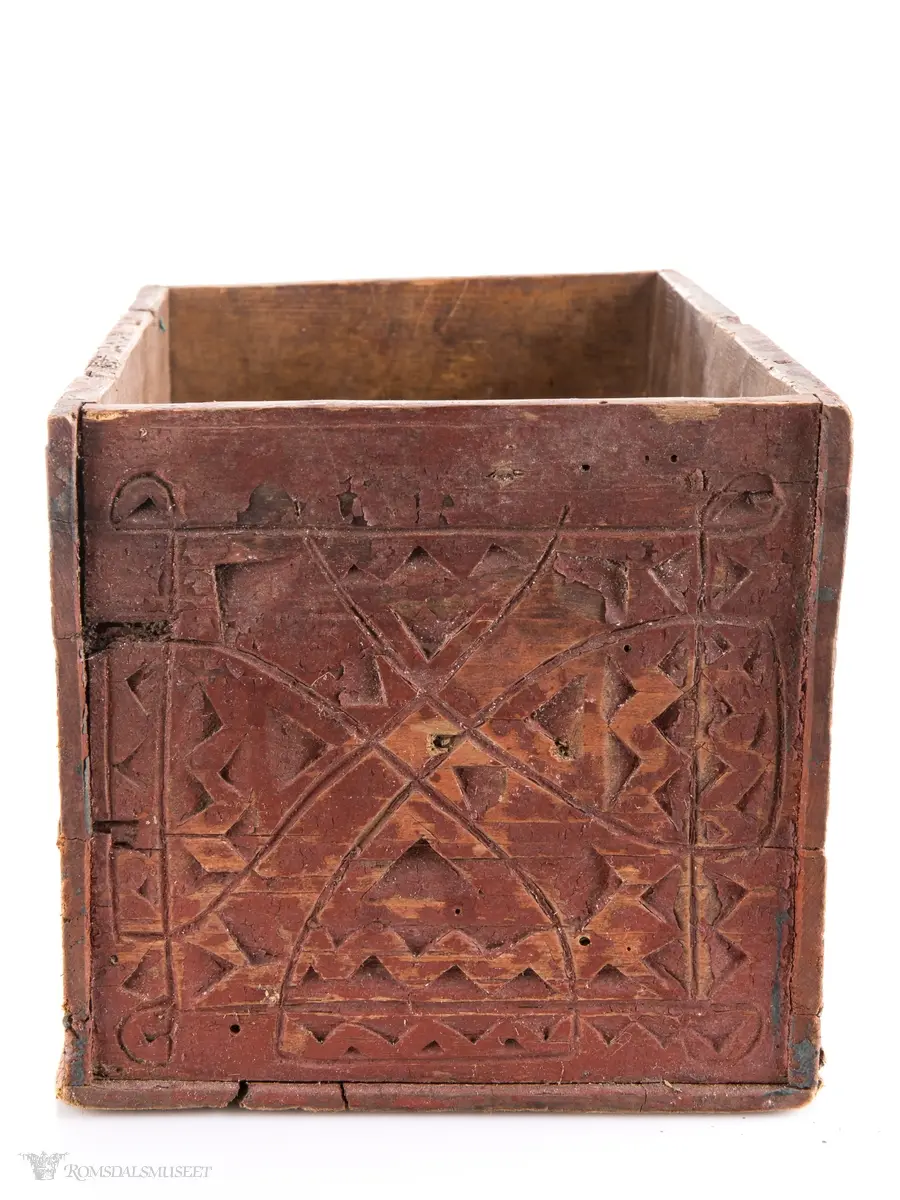 To sammenkomponerte seksbladsrosetter på hver langside. På kortsidene er det skåret ut fire klokkeformede strukturer fylt med spetter og border som til sammen ligner på et noe asymmetrisk solkors/kors.