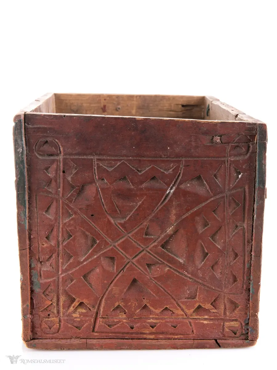 To sammenkomponerte seksbladsrosetter på hver langside. På kortsidene er det skåret ut fire klokkeformede strukturer fylt med spetter og border som til sammen ligner på et noe asymmetrisk solkors/kors.