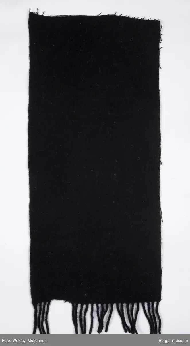 Ensfarget tekstilbit, med klippete kanter, ene kortside med frynser.