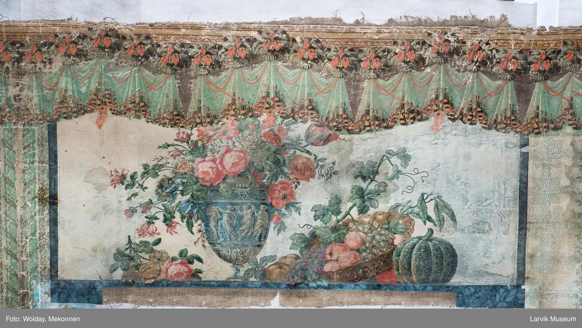 |Tapeten er påmalt tapetborder og brystning. Fra Hovland gård i Larvik.
Den øverste, brede borden: Gerlander/draperi med blomsterranker.
Den nederste, smalere borden: Tekstilbord med blomster. Øver døren til høyre: Stillebenmotiv med blomster og frukt.