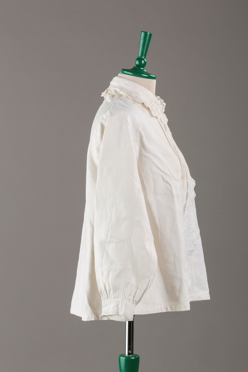 Form: Hoftelang trøye, Lange ermer, krage. Kragen og åpningen foran er kantet med  maskinprodusert blonde. Tre biser på hver side av åpn. foran. Lukkes med to løse knapper.