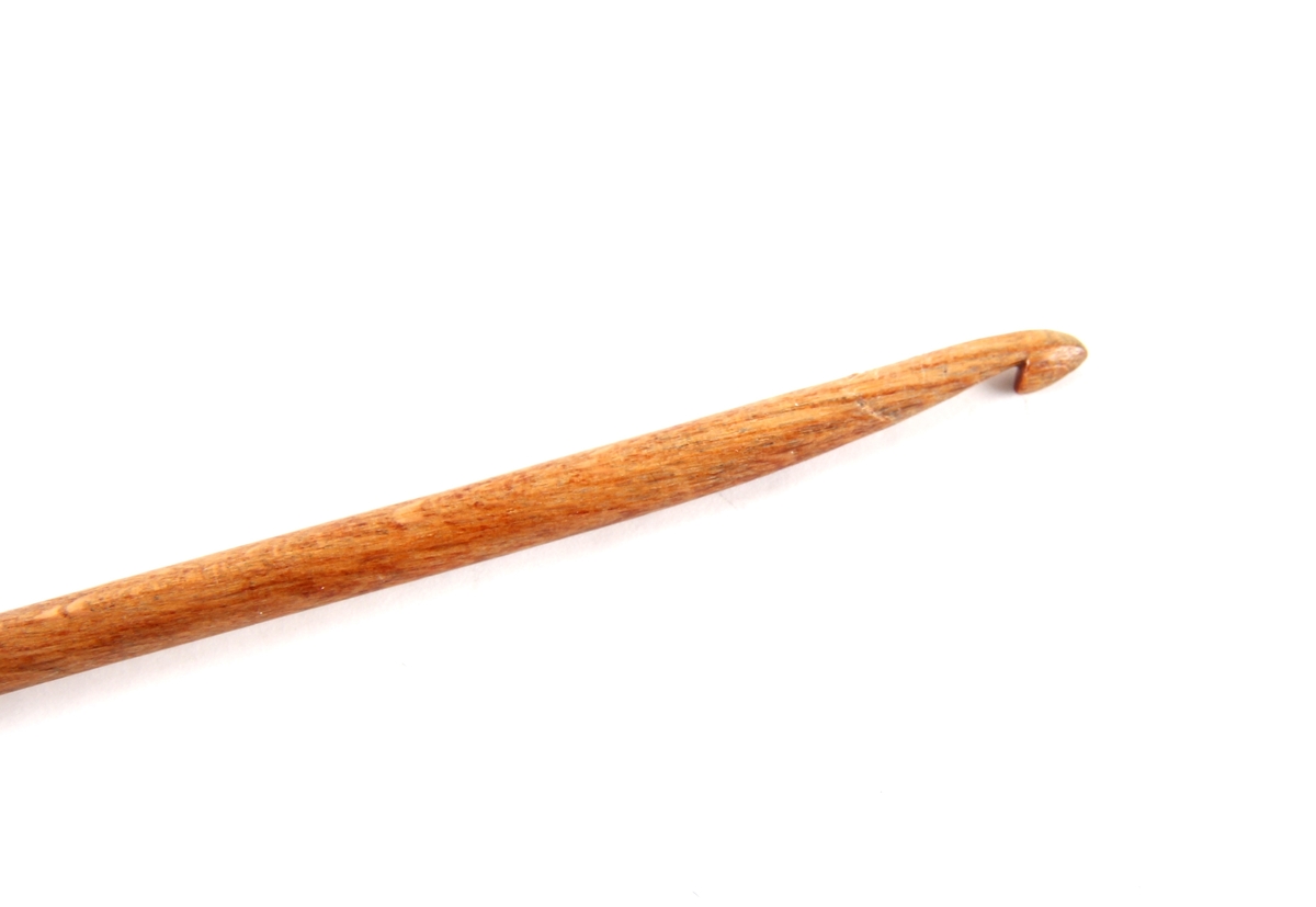 Lang heklenål av tre. Med en krok i ene enden og en rund knott i den andre.