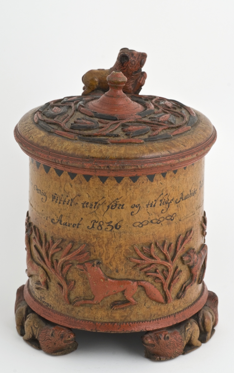 Dekorert med fortløpende billedfrise med dyr og trær på nederste del av korpus. Kannen har løveføtter og løvegjekk og bakkantine som håndtak. 