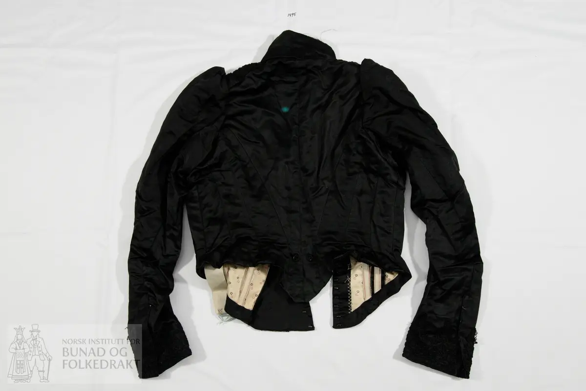 Kjoleliv til skjørt NBF2017-1494 i svart silkesateng med skrålagte folder og kjøpeblonder i svart.  Foret med trykt bomullsfor. Tilbaketrukne sidesømmer og søm midt bak. Tosømsermer. Tre og to spiler på hver side midt framme. Tre spiler på hver side av ryggen (i sidene). Høy krage i halsen, som er avrundet ned mot midt framme. Lukking midt framme med en tett rekke hekter, 24 stk. Tre legg og en bred blondekant på skrå over brystet. Skrå lukning med overlivet på venstre side. Fire hekter har trolig vært festet på i tråhemper på høyre side av livet, på skrå. Noen rester er så vidt synlige. Livet er trolig ikke omsydd. Livet har i siste del av bruken vært brukt nedi skjørtet, tydelig på grunn av bøy i spilene og de to øyehektene midt bak på livet hvor stakken/køen har hengt. Rynket ermetopp. 
Ermene har påsydd blonde som mansjett, og har splitt med hekter til knepping.