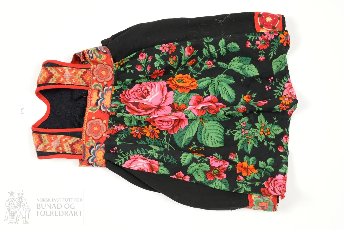 Liv sauma av fast tjukk mørk blå vadmål, påsett kelimvovne band som kryssar midt bak på ryggen. Kanta med raude kypertvovne ullband. Heile livet maskinsydd. 
Stakk sauma av krosskypertvove svart tynt stoff av syntetisk materiale. Stakken har løpegang med snøring oppe i livet. I nedkant og øvrekant er påsydd raude ullband med plattsaumsroser av anelinfarga ullgarn. Bandet oppe i livet er kun fastsydd i øvrekant og ligg laust utanpå stakken. 
Forkle fastsydd til det broderte ullbandet, av trykt kypertvove ullmusselin. 
Heile stakken maskinsydd.