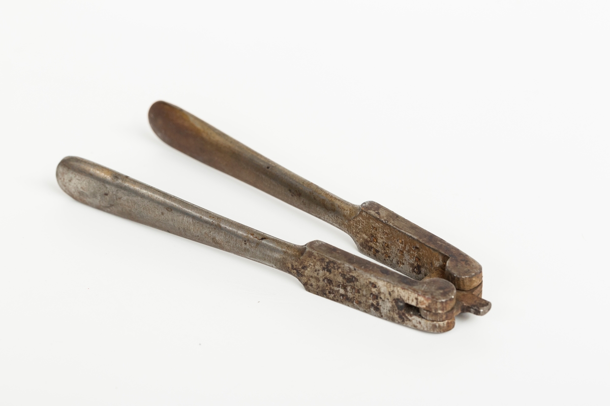 Nøteknekker i stål uten dekor. Utslåtte knaster på "gripeflatene". Hengsel med avstandstykker for to knekkeavstander.