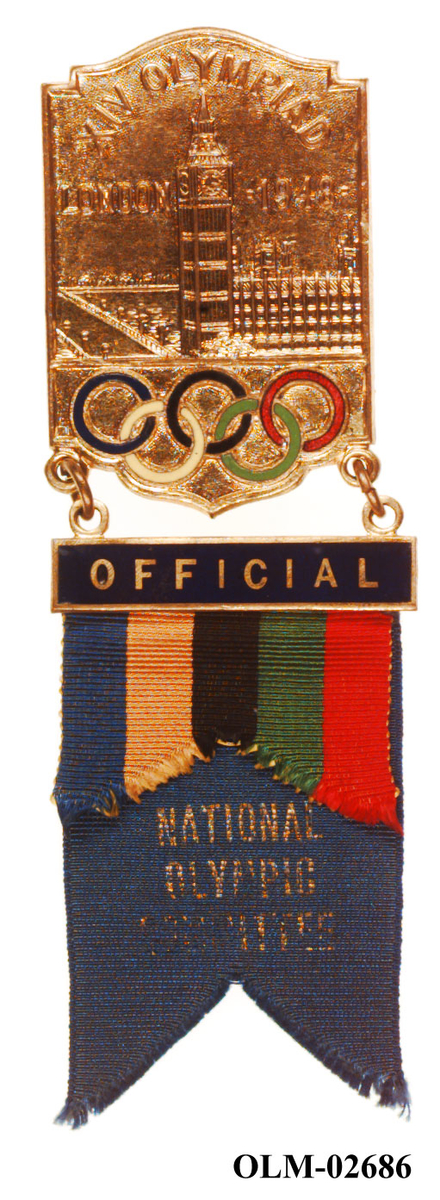 To-delt badge i metall og tekstil for Den Nasjonale Olympiske Komité. Metallmerket viser Big Ben i The Houses of Parliament med de olympiske ringene i farver. På den mørkeblå tekstildelen er det festet et bånd med farvene til de olympiske ringene.