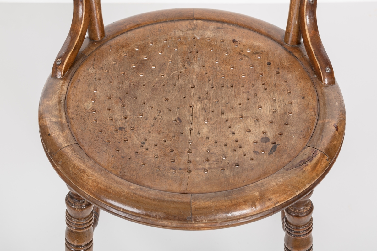 Stol i lakket treverk. Rundt stolsete med hullemønster. Rygg som er svakt buet med spiler og mønster. Dreide ben og spiler i rygg.