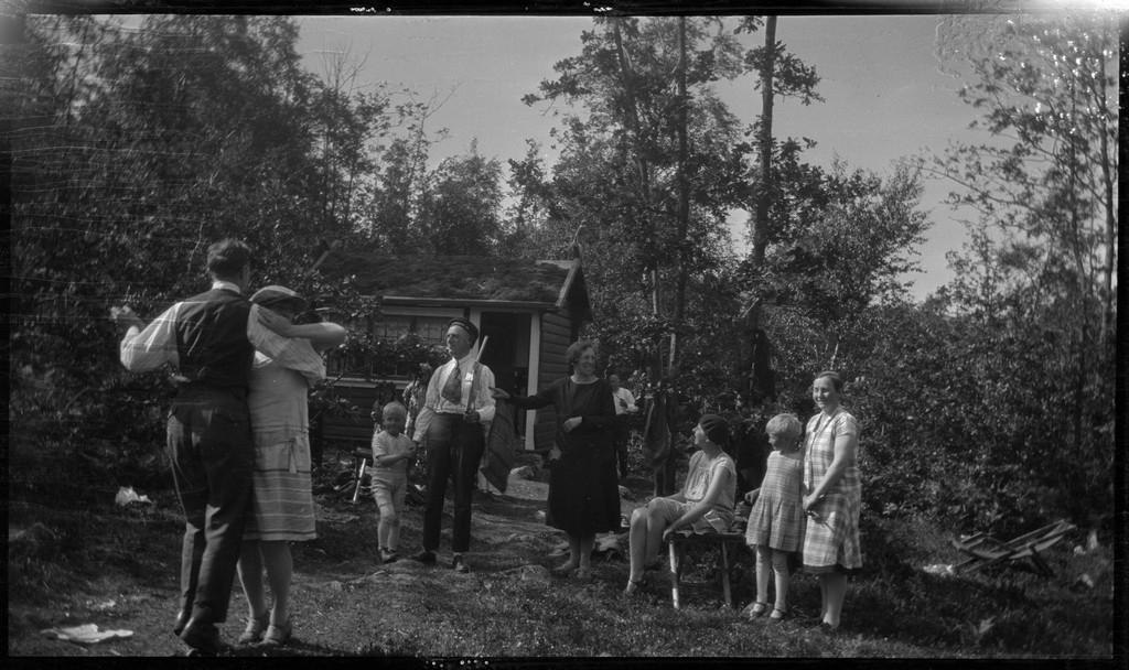 Selskap ved ei hytte i skogen. Familiene Torgrimsen, Johannessen og Jensen deltar. To personer danser. Frida Johannessen står midt i bildet i svart kjole.