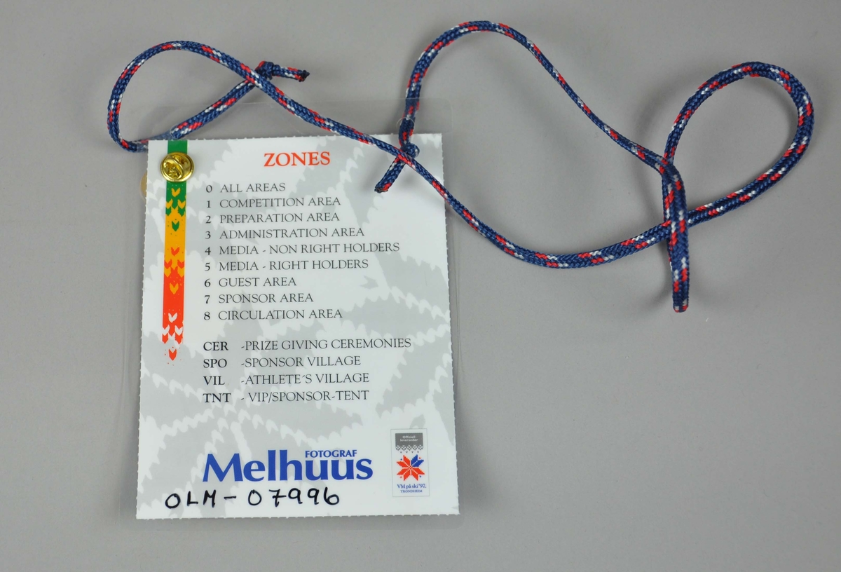 Enkelt akkrediteringskortfestet i blått bånd med røde og hvite dotter.Det er et farvefoto av Jan Staubo i front.En pins med innskrift " VMbyen-VM på ski'97 Trondheim " er festet foran på kortet.