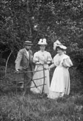 Gruppe, mann til venstre, to kvinner til høgre, står ute. Fr