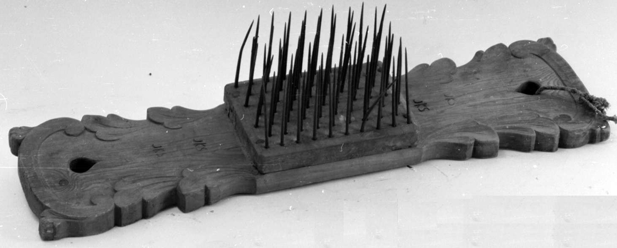 Linehkle av tre med bladutskjæringer. På midten er det festet en trekloss med stålnagler.