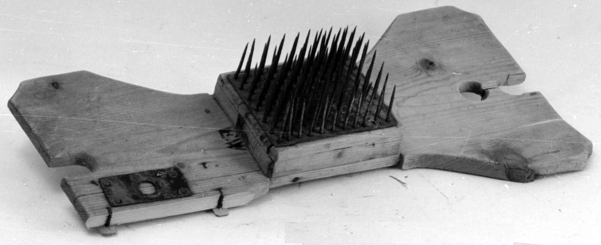 Linhekle av tre som er smalere på midten av brettet. Her er det festet en trekloss med stålnagler. Brettet er skadet.