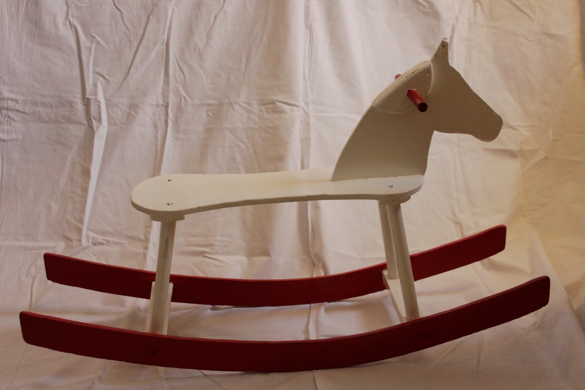 Enkel gunghäst i trä med medar. Hästen är vitmålad och handtag samt medar är röda. Målad med lackfärg.