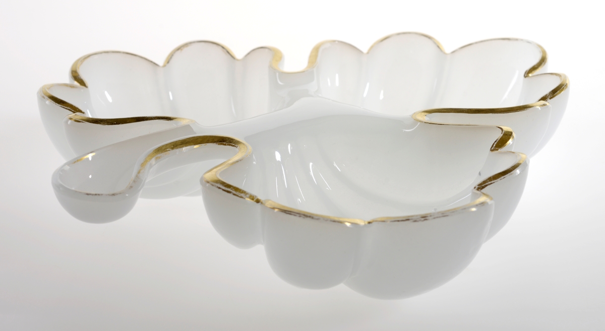 Skål av hvitt glass (opalinglass) formet som et eikeblad, med tre deler som former hver sin adskilte skål. Gullmalte kanter.