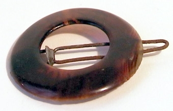 Runt hårspänne tillverkat av celluloid, på baksidan finns en nål av metall för fastsättning.