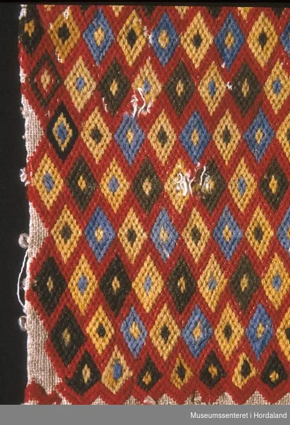Bringeklut brodert med diamantmønster i raud, blå, gul og brun farge.