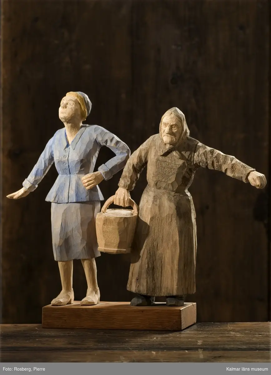 KLM 43830:13 Skulptur, av trä. Benämnd, Mor och dotter. Datering, 1950-tal. Signatur, HR. Figuren består av en gammal kvinna i brunbetsade kläder och schalett om huvudet, hon bär en hink i ena handen. Bredvid henne står en yngre kvinna i blåbetsad dräkt. Figurerna är monterade på en träplatta.