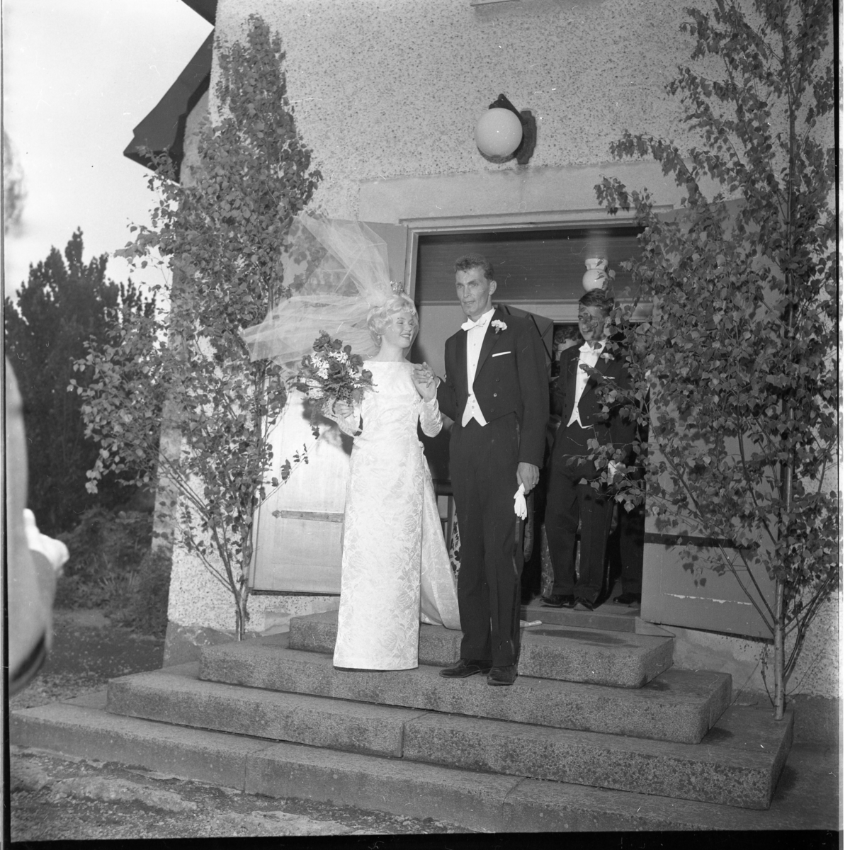 Nygifta Rolf Nilsson och Lisbeth Johansson utanför Örserums kyrka. Vinden sliter i brudslöjan.